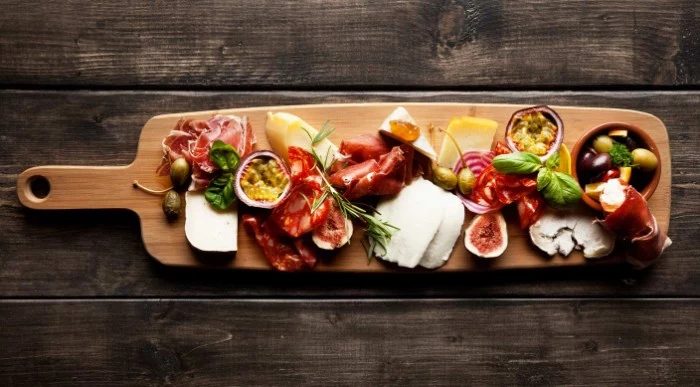 long wooden board, with feta cheese, passion fruit and figs, prosciutto and salami, and many others hor dourves 