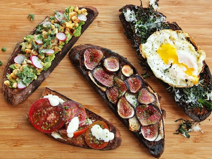 large slices of bread, covered with different toppings, hor d oeuvres with guacamole and radish, tomato and mozzarella, figs and egg