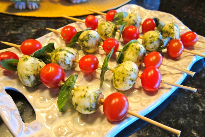 pesto-covered mozzarrella and cherry tomatoes, skewered with fresh basil leaves, hour derves, on a ceramic decoartive board