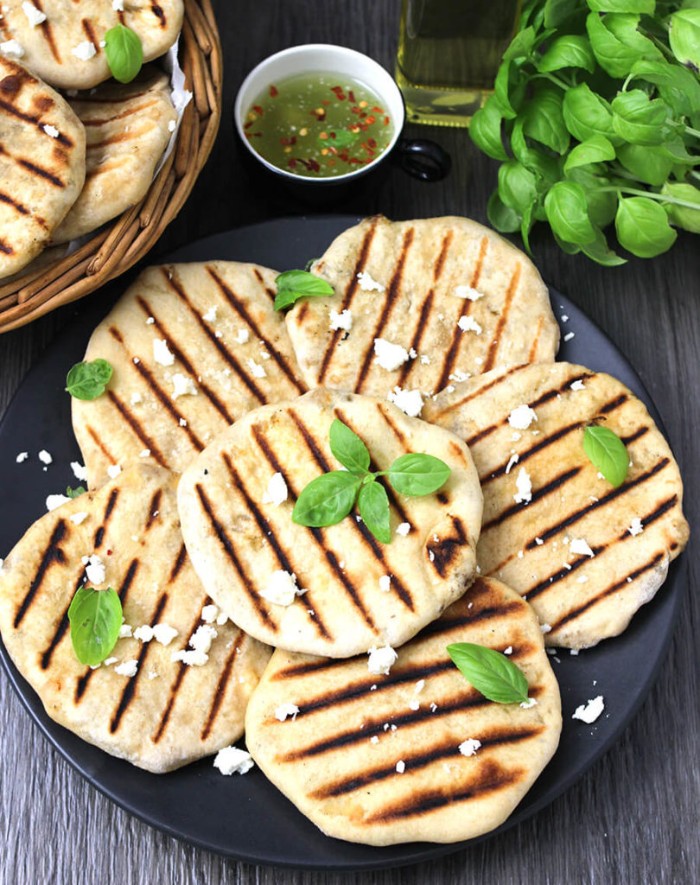 black plate containing several grilled flatbreads, topped with cheese and basil leaves, hor dourves, small dish with sauce nearby