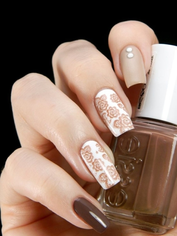 brown nail polish, in a small bottle, held by a hand, with long square nails, decorated with brown, white and nude nail polish, and flower shaped, nail decal stickers