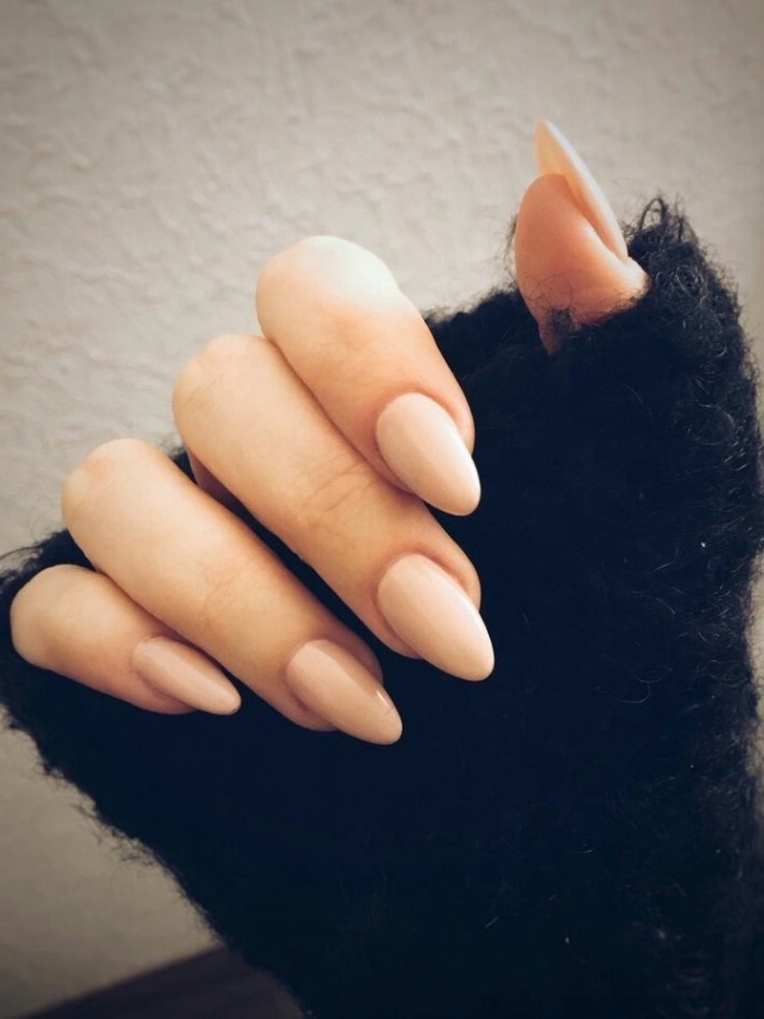 classic manicure with sharp, oval nails in pale pink, best nude nail polish, hand in a oversized, fluffy black sleeve