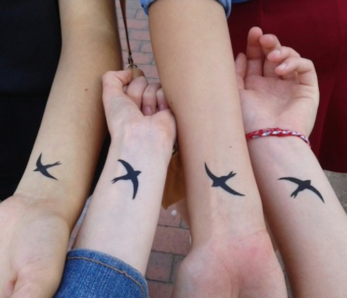 swallows in flight, done in black ink, on the wrists of four slim arms, placed next to each other, friendship tattoos