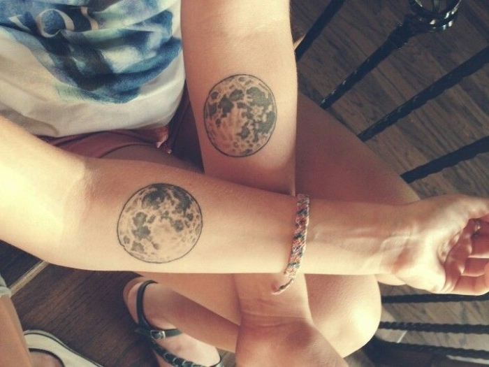 full moons done in grey ink, identical matching friend tattoos, bellow the crrok of the elbow, of two crossed arms