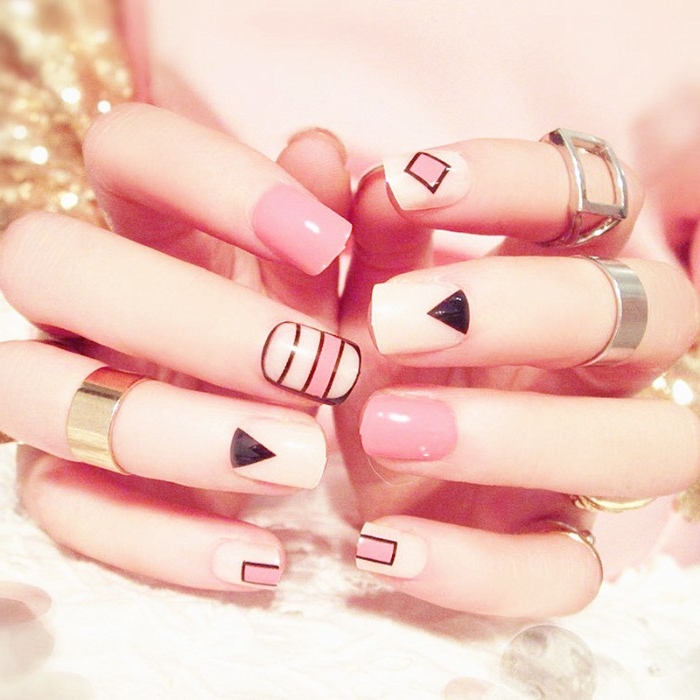 bubble gum pink nude nails, decorated with geometrical motifs, in black and white, on two hands with several rings