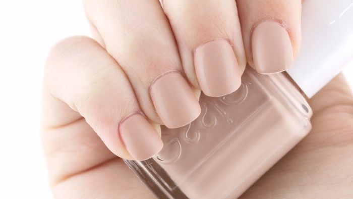 natural looking manicure, short and square nude matte nails, on a hand, holding a bottle of nail polish