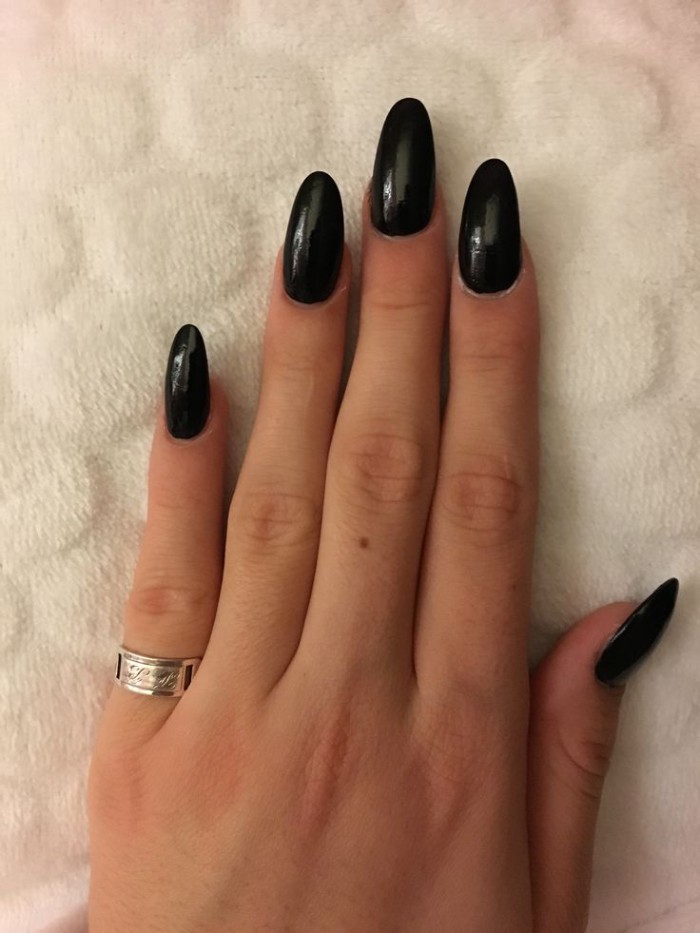 shiny black nail polish, on five long acrylic nails, attached to a hand with slender fingers, resting on a white surface