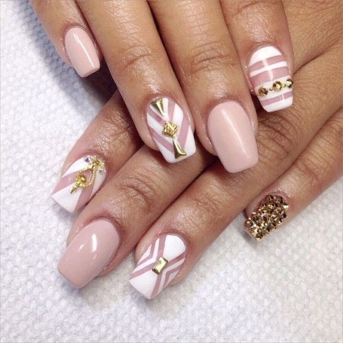stripes in white, and gold nail decal stikers, on a medium long, coffin shaped manicure, with nude pink nail polish, on two hands, placed on a white surface