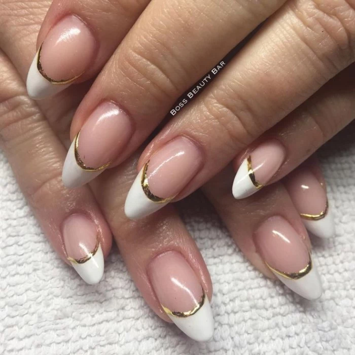 french manicure with gold details, on two pale hands, with medium to short pointy nails