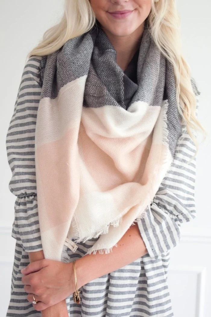 close up of a grey, white and pale pastel pink scarf, draped around the neck of a smiling, young blonde woman, how to wear a blanket scarf, with a striped blouse