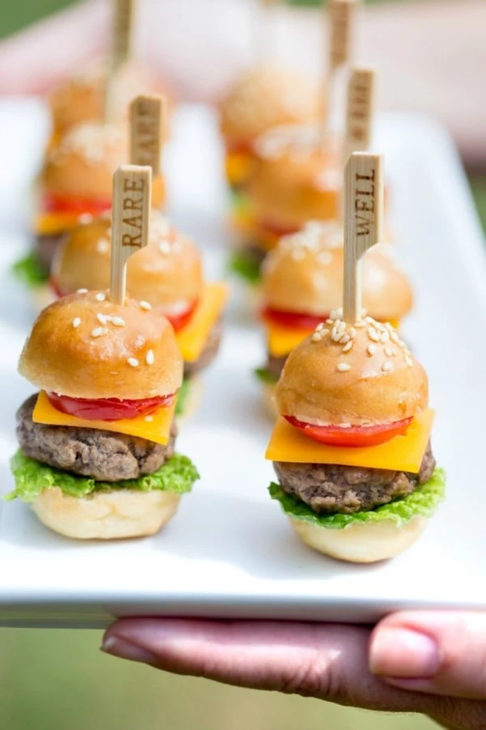 bite-sized hamburgers, on a white rectangular plate, horderves ideas. each burger contains a wooden cocktail stick, saying whether it's rare, or well done