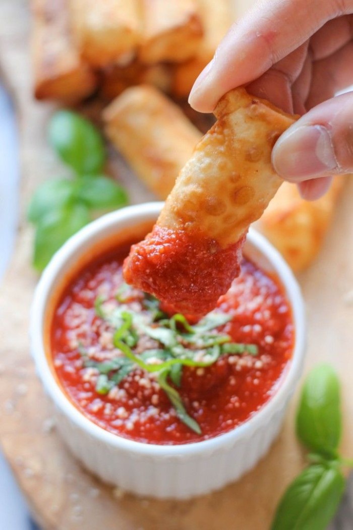 spring roll dipped in red sauce, held by a hand, over a white dish, filled with salsa, and topped with chopped green herbs