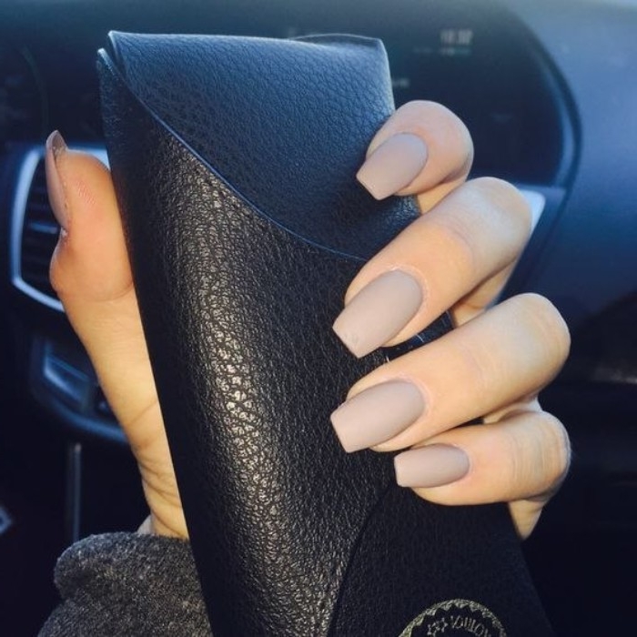 greyish-beige matte nail polish, on a square manicure, worn by a hand, holding a textured, black leather glasses case