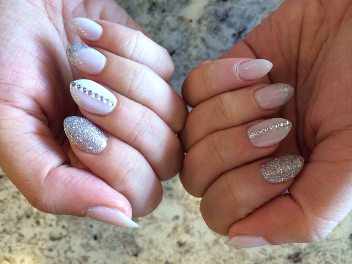 glitter in silver, and matching rhinestones, decorating the white, short stiletto nails, of two hands