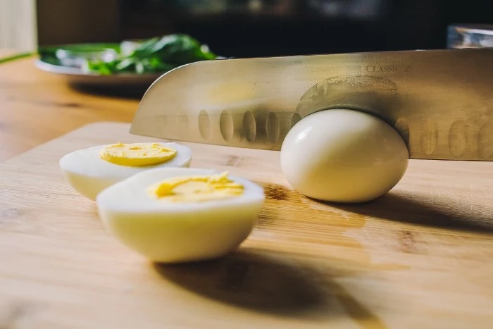 knife cutting through a hardboiled egg, how to make horderves, two halves of another egg nearby