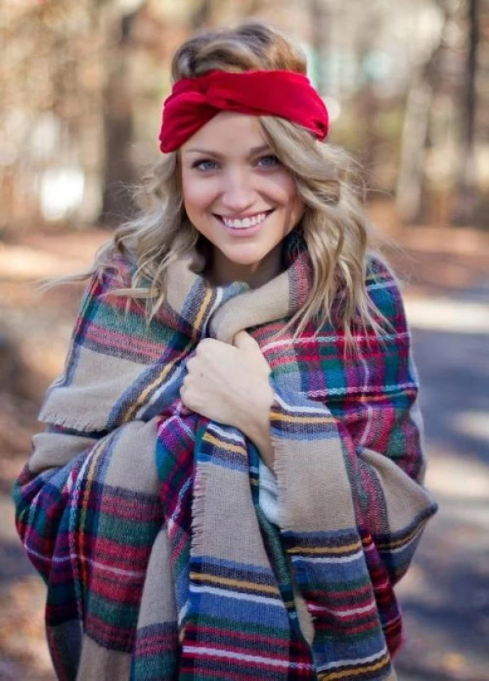 bright red headband, worn by a smiling, young blonde woman, bundled in an oversized, multicolored plaid shawl, how to fold a blanket scarf, when it's really cold