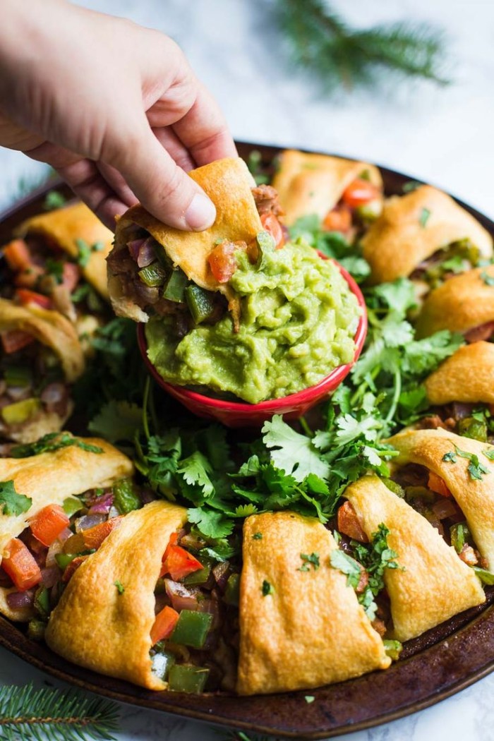 bread stuffed with vegetables, on a large round plate, with a dish of guacamole in the middle, hour derves, hand dipping a piece of bread in the guacamole
