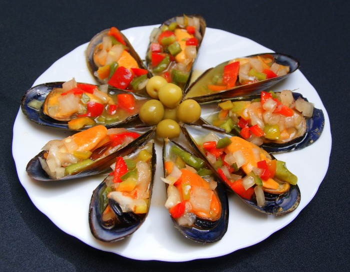 mussels cooked in their shells, with chopped vegetables and green olives, hor dorves, served in a round plate