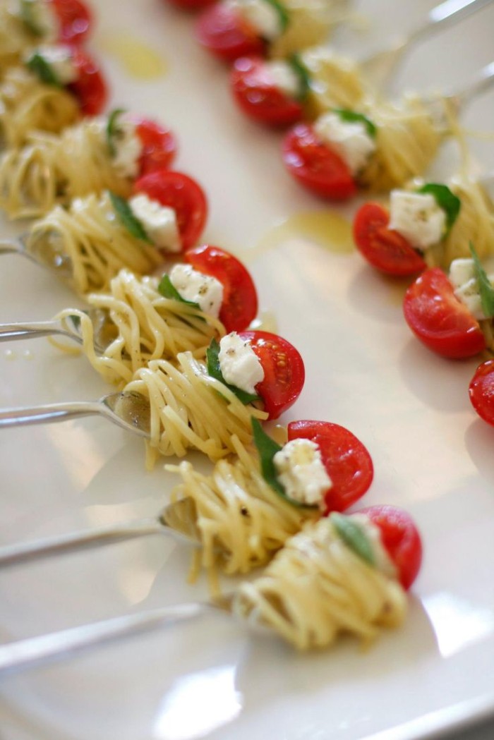 spaghetti wrapped around several forks, and topped with fresh basil leaves, cheese and cherry tomatoes