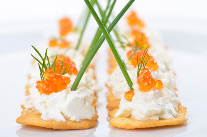 thin crackers with creamy, white spread and red caviar, hor dourves garnished with chives, and sprigs of dill