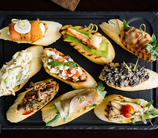 nine pieces of toasted bread, with different toppings, smoked salmon and boiled egg, grilled chicken and cherry tomato, and many others