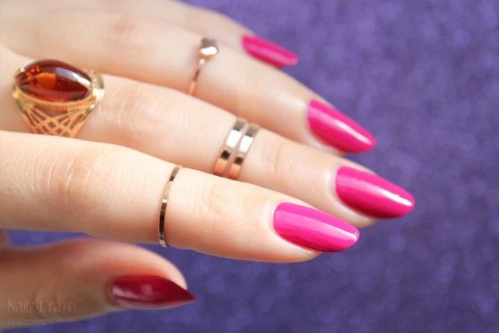 oval shaped nails, in hot pink, on a pale hand, with several golden rings, one of which features a large amber stone