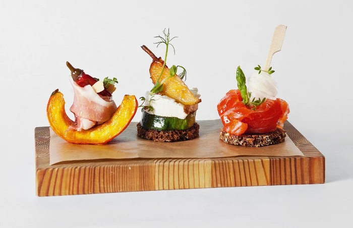 thick wooden block, with three artisan canapes, baked peach with prosciutto, tomato with asparagus, pear with ricotta, appetizers for a crowd