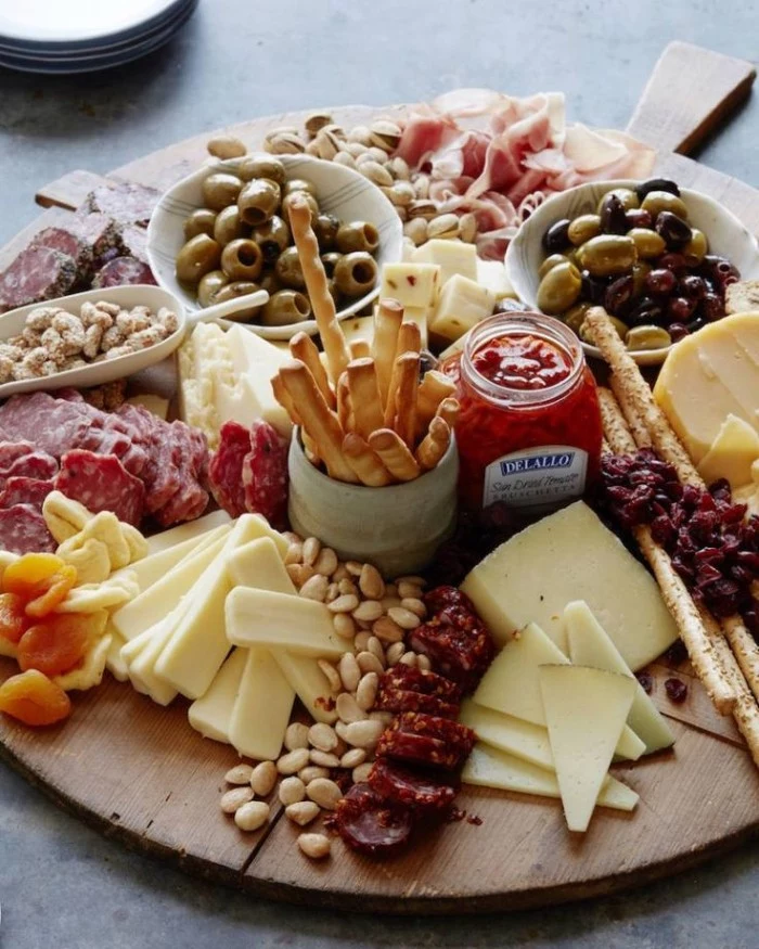 bread sticks and nuts, salami and cheeses, on a big round wooden platter, with dried fruit olives, and different dips
