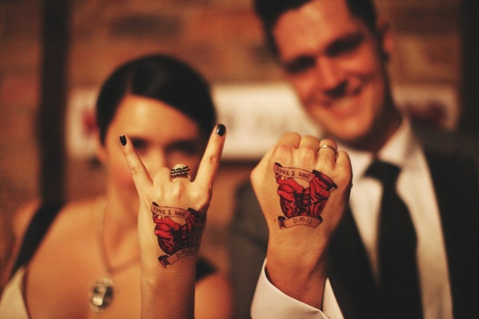 smiling couple in formal attire, showing the backs of their hads to the camera, they have identical tattoos, in black and red and yellow, husband and wife tattoos