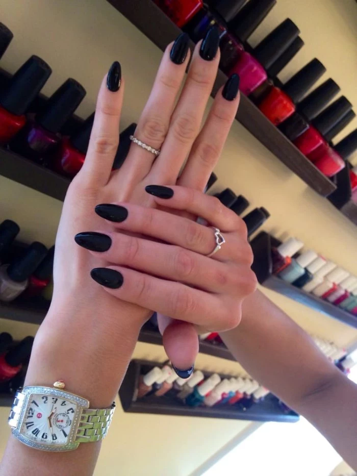 watch and two rings, worn by two slim hands, with long fingers, and a long oval manicure, painted in black nail polish
