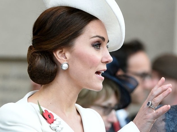 white hat and coat, decorated with a red poppy badge, worn by kate middleton, hand with a large ring, and nude nails