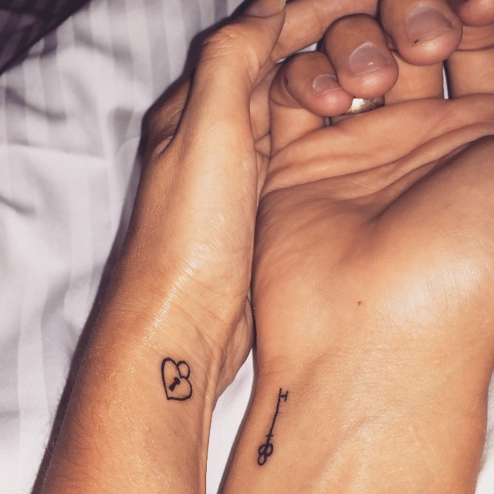 very small heart-shaped lock, tattooed on the wrist of a hand, matching tattoos, another hand nearby with a key, tattooed on its wrist