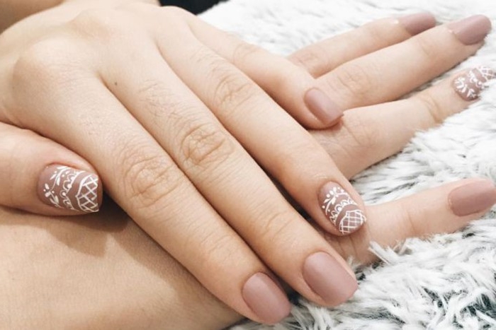 ash pink nail polish, with white lace-like, hand-drawn motifs, on nude matte nails, attached to two pale hands