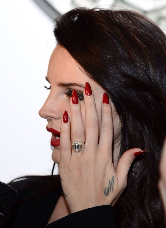 blood red glossy nail polish, on acrylic nail shapes, worn by lana del ray, with dark brunette hair, and bright red lipstick