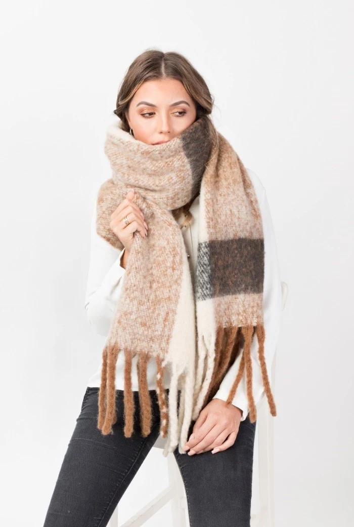 fluffy and soft, oversized beige woolen scarf, with white and grey pattern, and long brown tassels, wrapped around the neck and mouth, of a young brunette woman