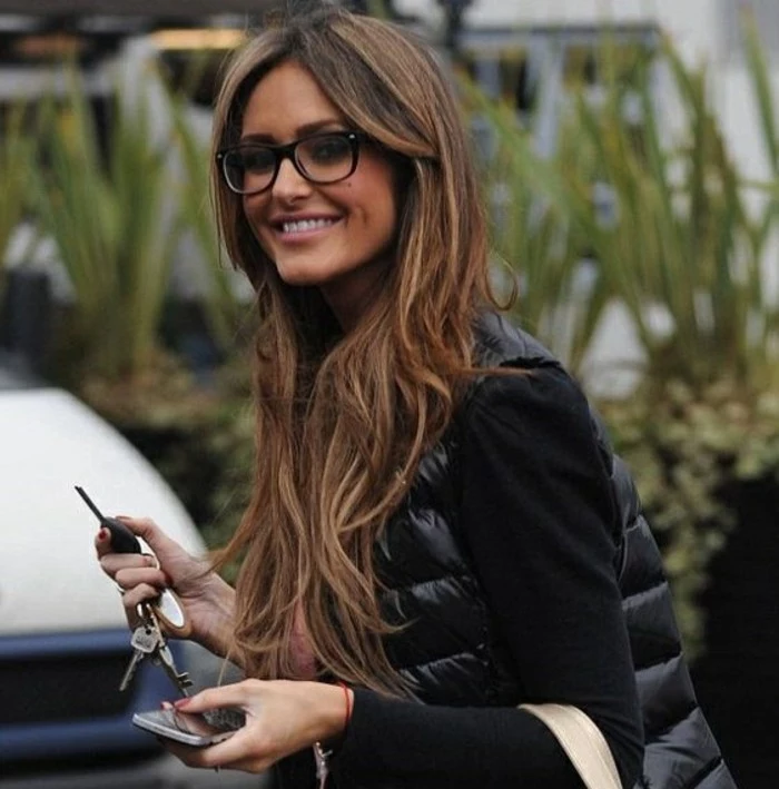 smiling slim woman, dressed in black, and wearing black-framed glasses, long balayage dark hair with layers