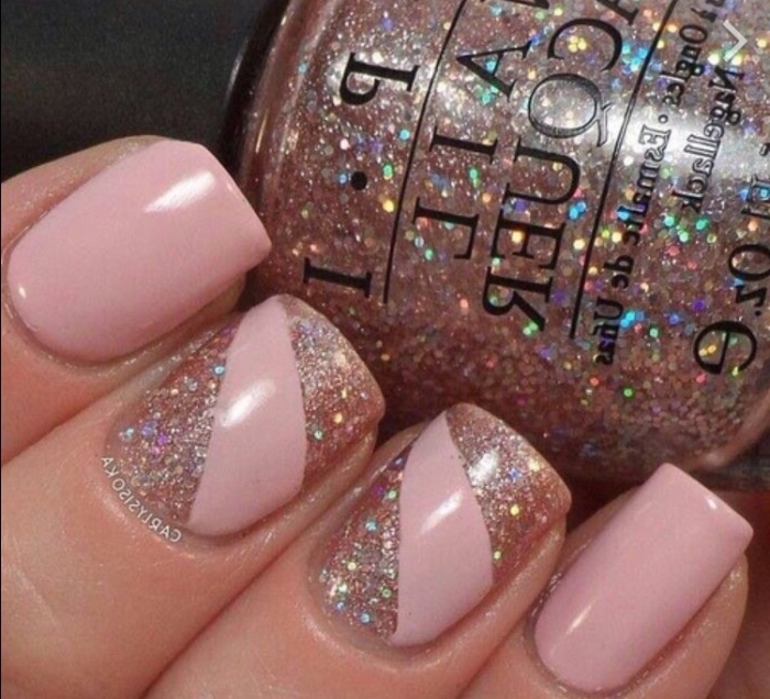 glass bottle of glitter nail polish, held by a hand with square nails, painted in nude pink, and decorated with multicolored glitter