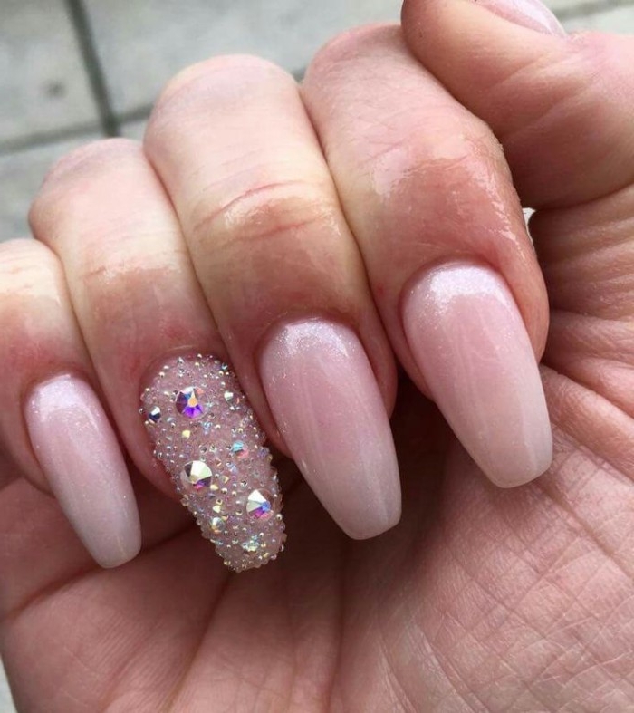 slightly sparkly nude pink nail polish, on coffin shaped manicure, the ring finger nail is covered in 3D, gem decal stickers