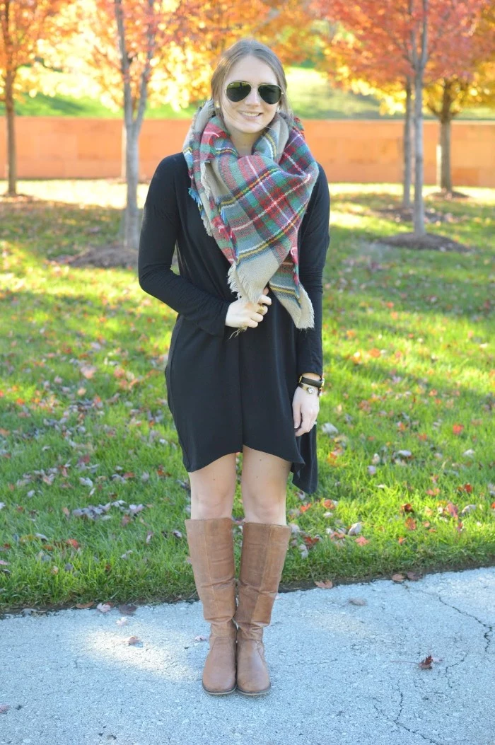 mini dress in black, worn with brown leather boots, and a checkered scarf, by a smiling blonde woman, with dark sunglasses, ways to wear a blanket scarf, fall scene in the background
