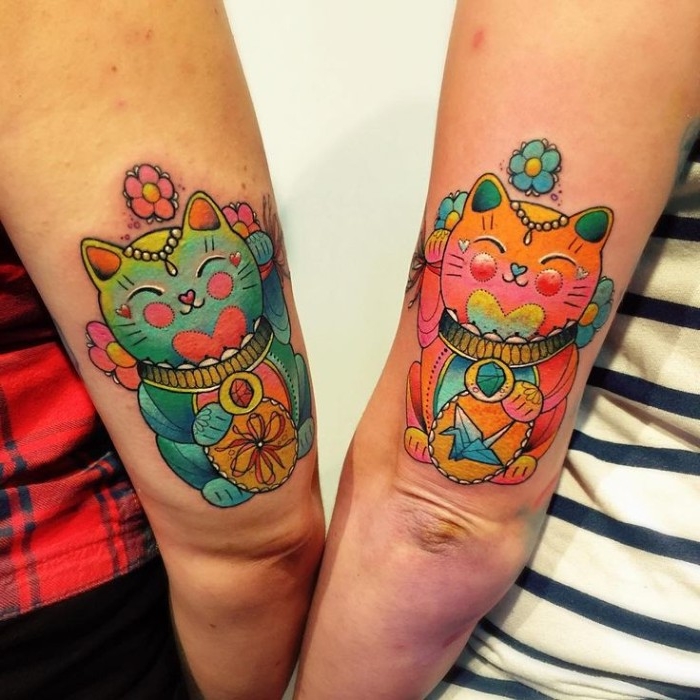 japanese-inspired waving cat tattoos, identical maneki-neko design, done in different colors, above the elbows of two arms