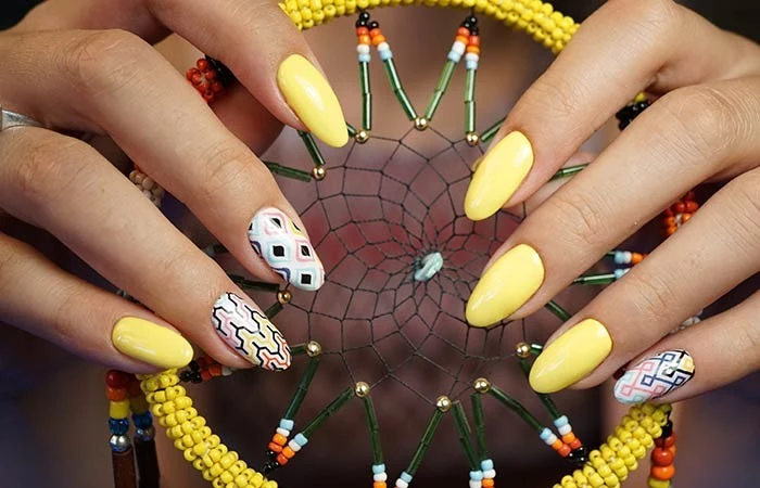 yellow acrylic nail shapes, some decorated with colorful patterns, on two hands, holding a dream catcher