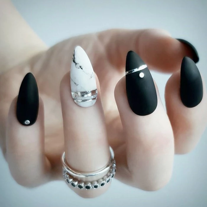 matte black stiletto nails, decorated with rhinestones, and metallic silver stripes, the ring finger nail features a marble-like design
