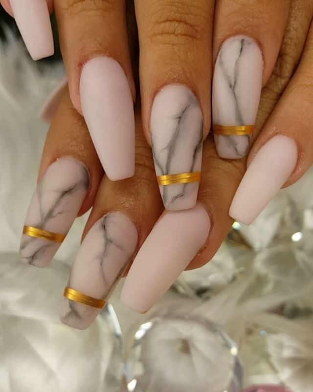 nude matte nails, with long ballerina shape, four decorated with a grey, marble-like pattern, and gold stripes, and four left plain