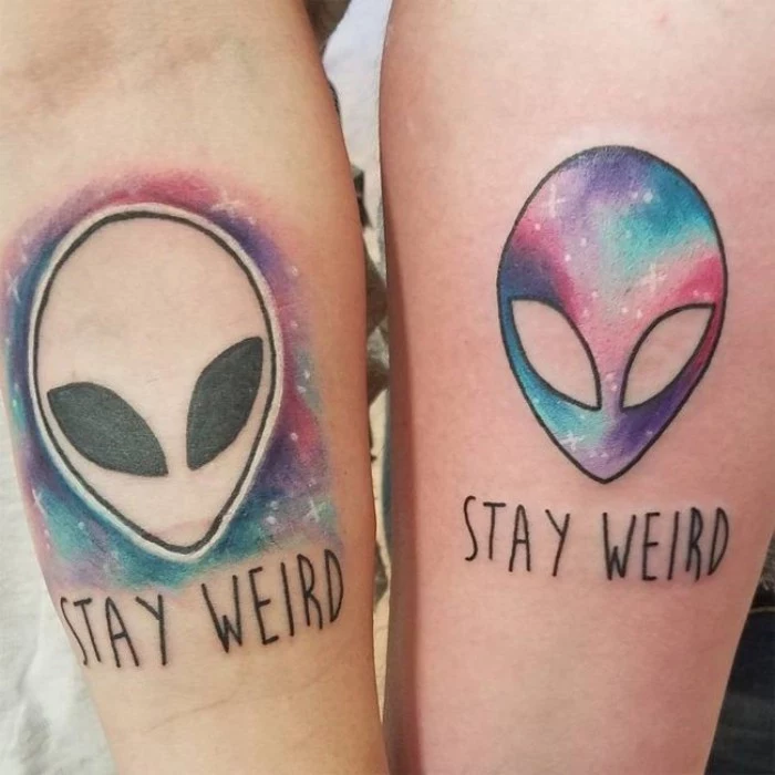 stay weird tattooed on two arms, under pictures of aliens' heads, done in black and multicolored ink, matching bestfriend tattoos, galaxy watercolor effect