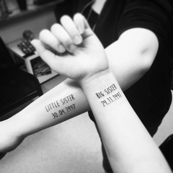 arms with black tattooes, one saying little sister, and the other sayng big sister, each one features a different date, matching sister tattoos