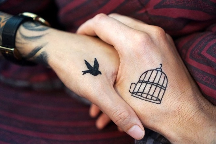 bird in flight, tattooed in black on a hand, held by another hand, with a black bird cage tattoo, matching tattoos with symbolic meaning