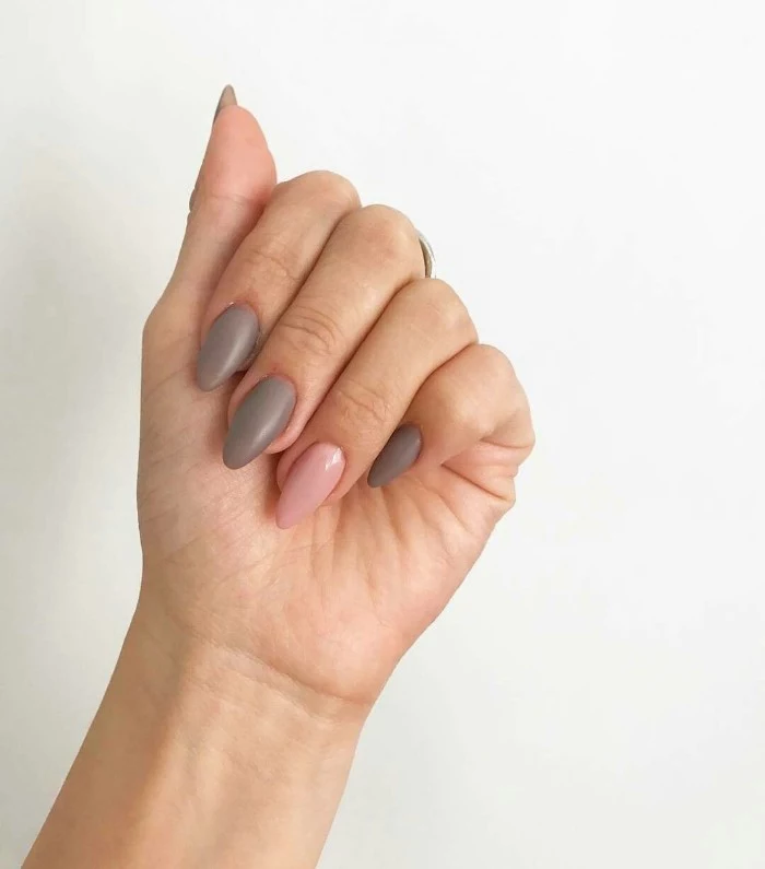 hand with folded fingers, and medium to short pointy nails, painted in creamy grey, and pastel pink nail polish