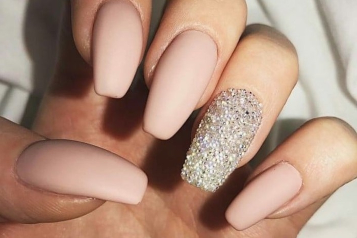 nude nails with glitter, long ballerina shape, and pale pastel pink matte nail polish, on a hand with folded fingers