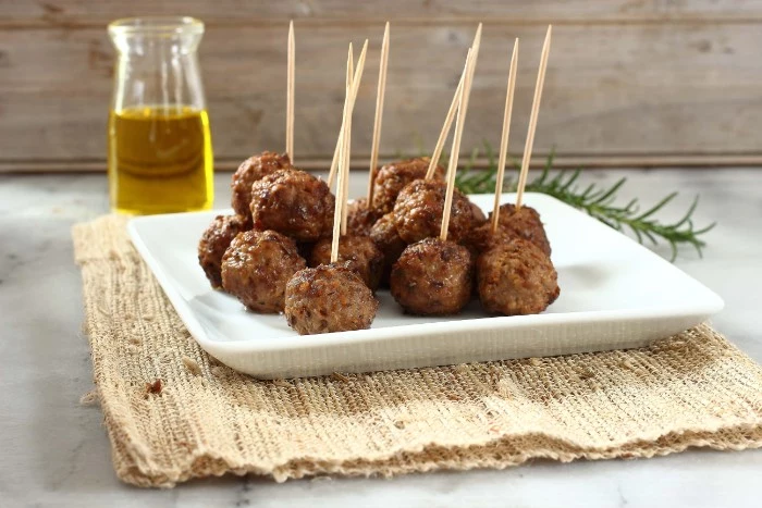 cocktail meatballs on a white dish, hor d oeuvres with meat, a clear bottle of olive oil in the background