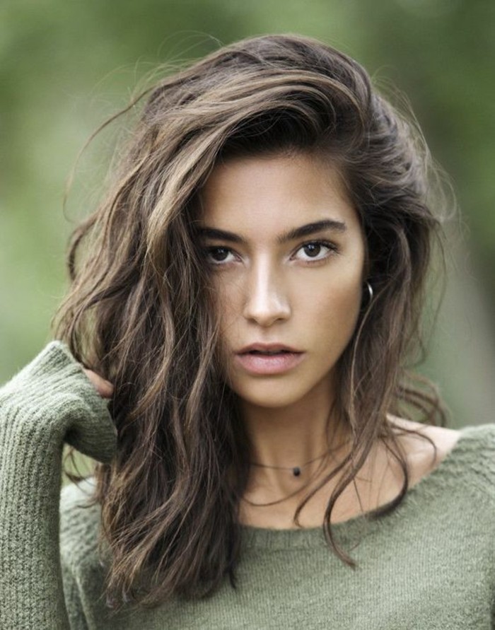 olive green sweater, worn by a dark-eyed young woman, with messy brunette hair, swept over to one side, balayage brown hair, windswept wavy look
